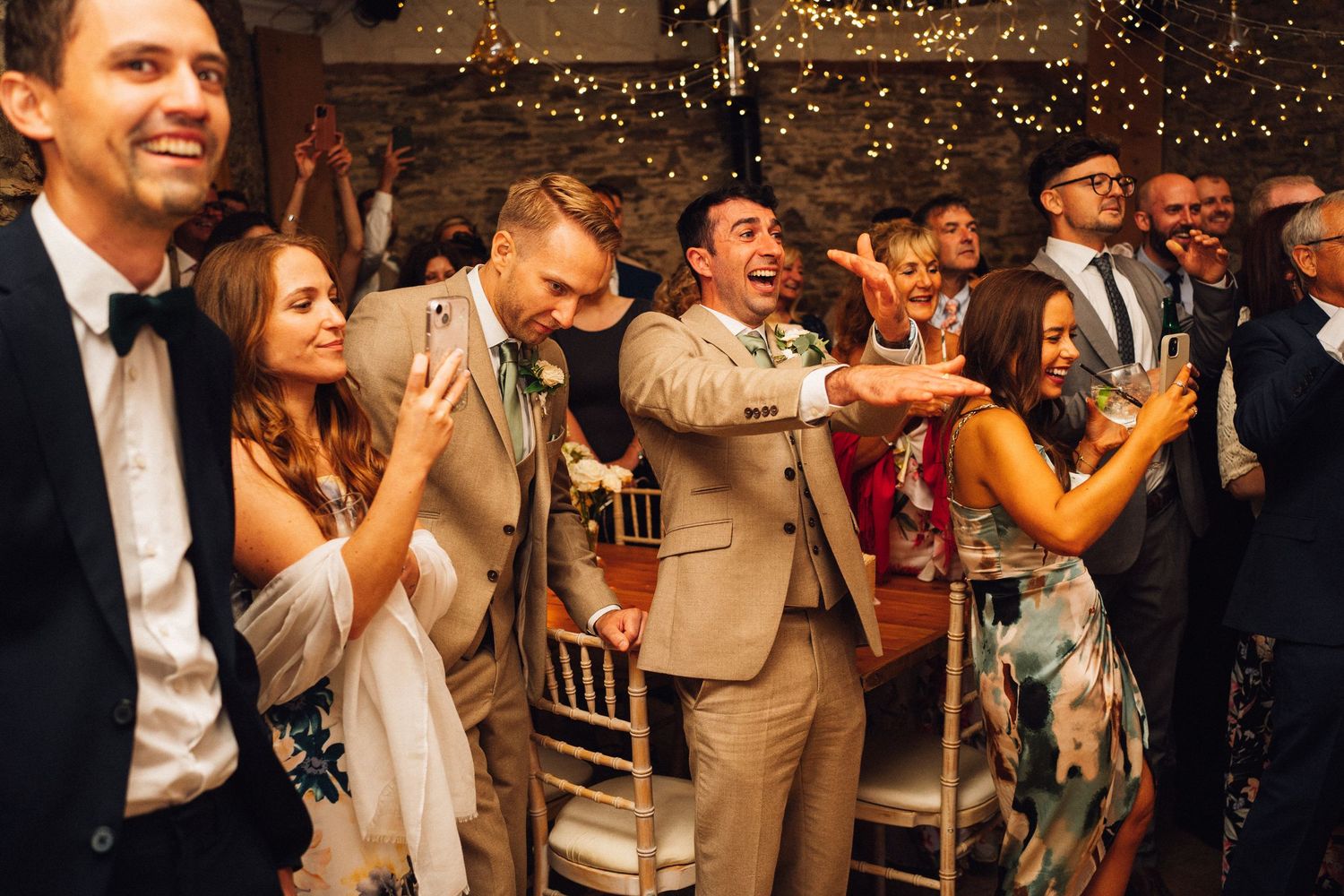 Wedding guests laughing and clapping during celebration with confetti falling.