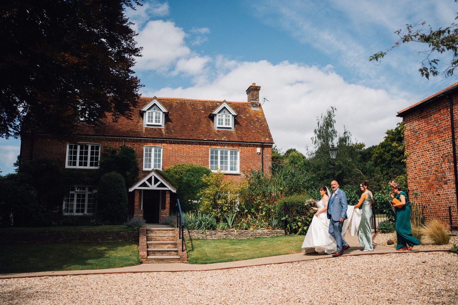 A panoramic view of a rustic brick farmhouse venue with gravel driveway and surrounding greenery.