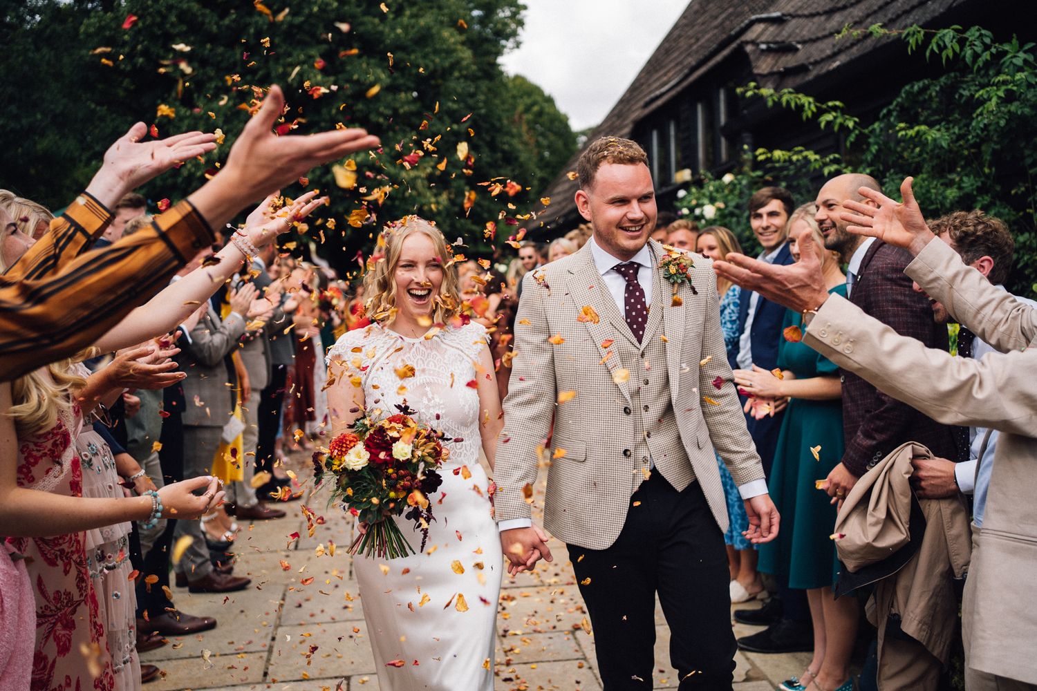 Wedding guests shower newlyweds with flower petals during a joyful outdoor celebration at a rustic venue.