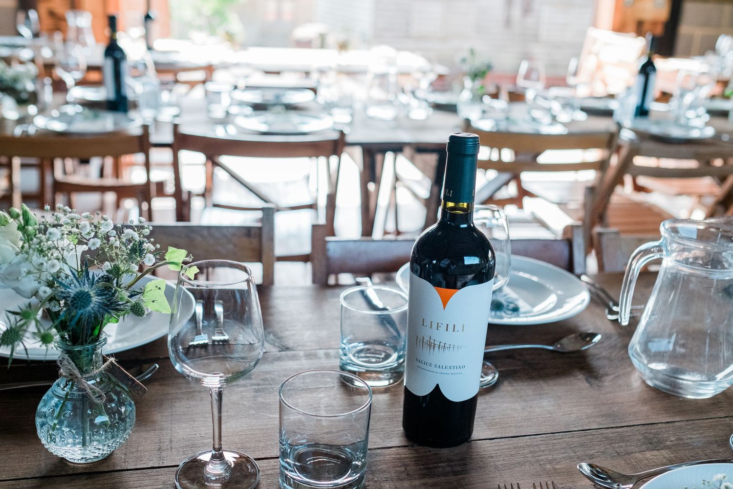 Elegant table settings with wine glasses and floral centerpieces arranged on wooden tables in a rustic venue.
