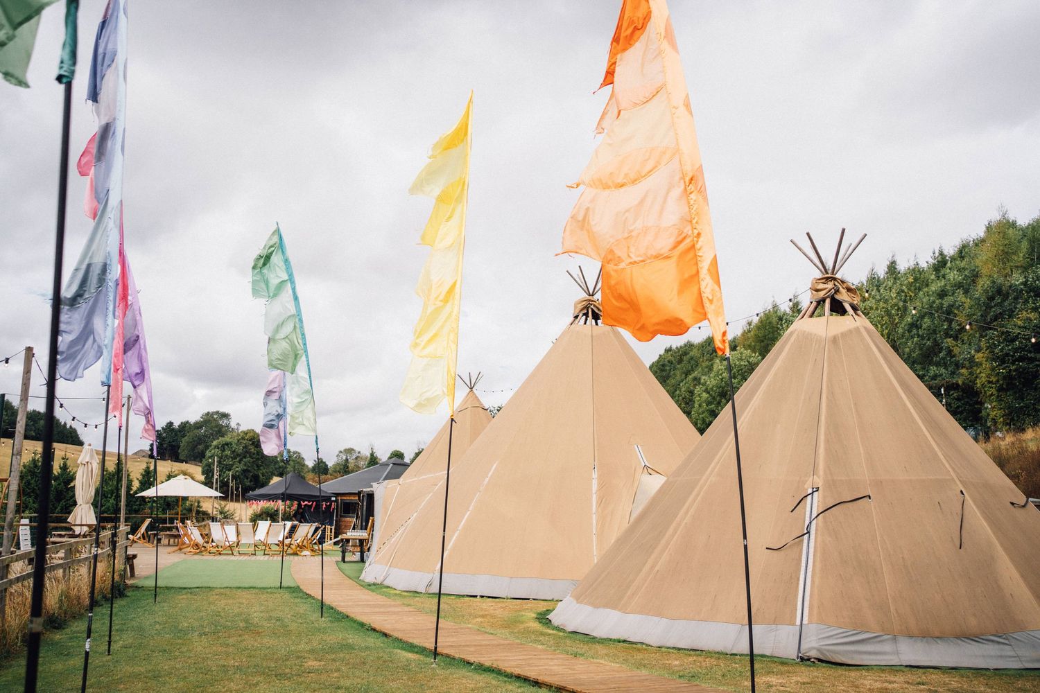 Row of traditional teepee tents with colorful flags waving in the wind at an outdoor festival gathering.