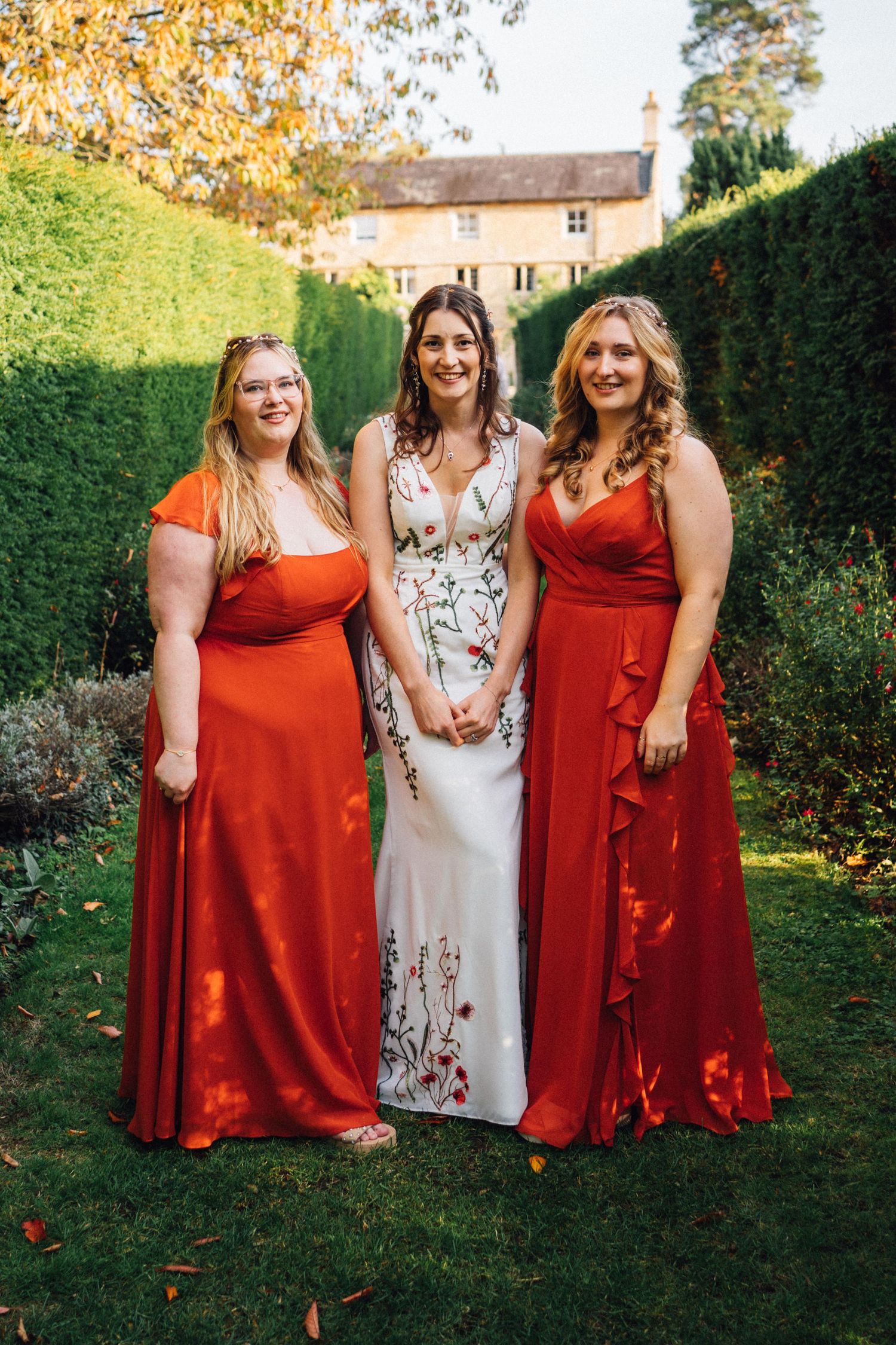Bridesmaids in red dresses and one in floral print pose together in a garden setting.