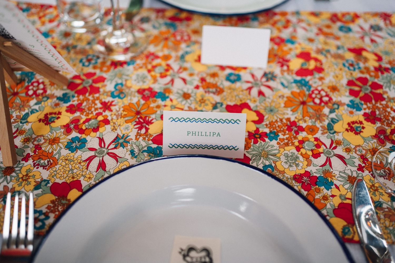 Place settings with white plates on vibrant floral print tablecloths at a wedding reception.