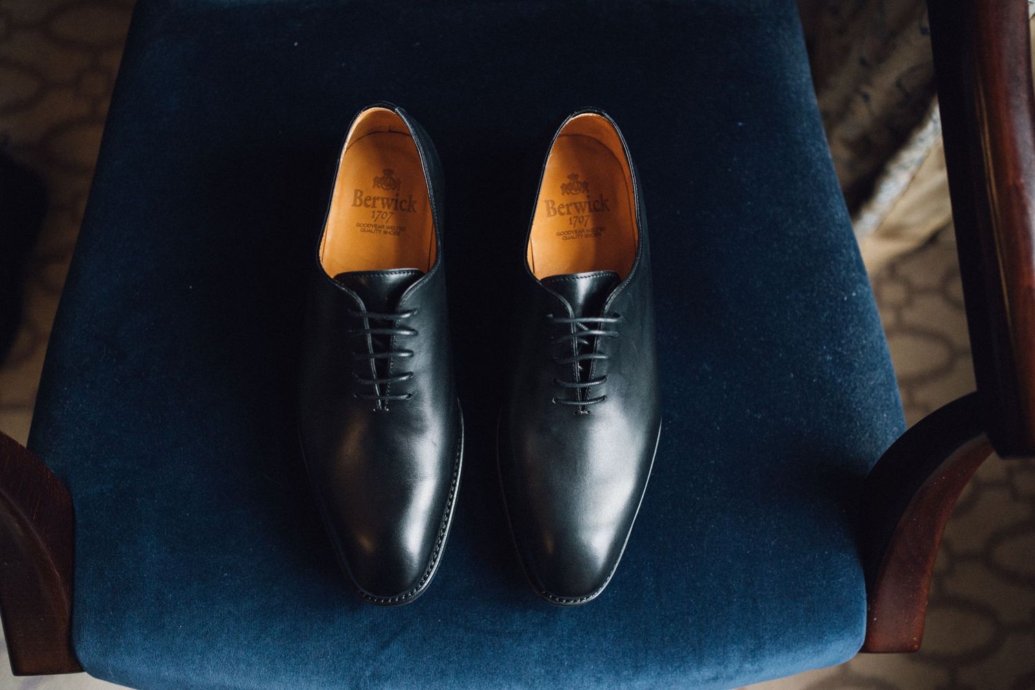 Polished black formal dress shoes displayed on a navy blue velvet chair.