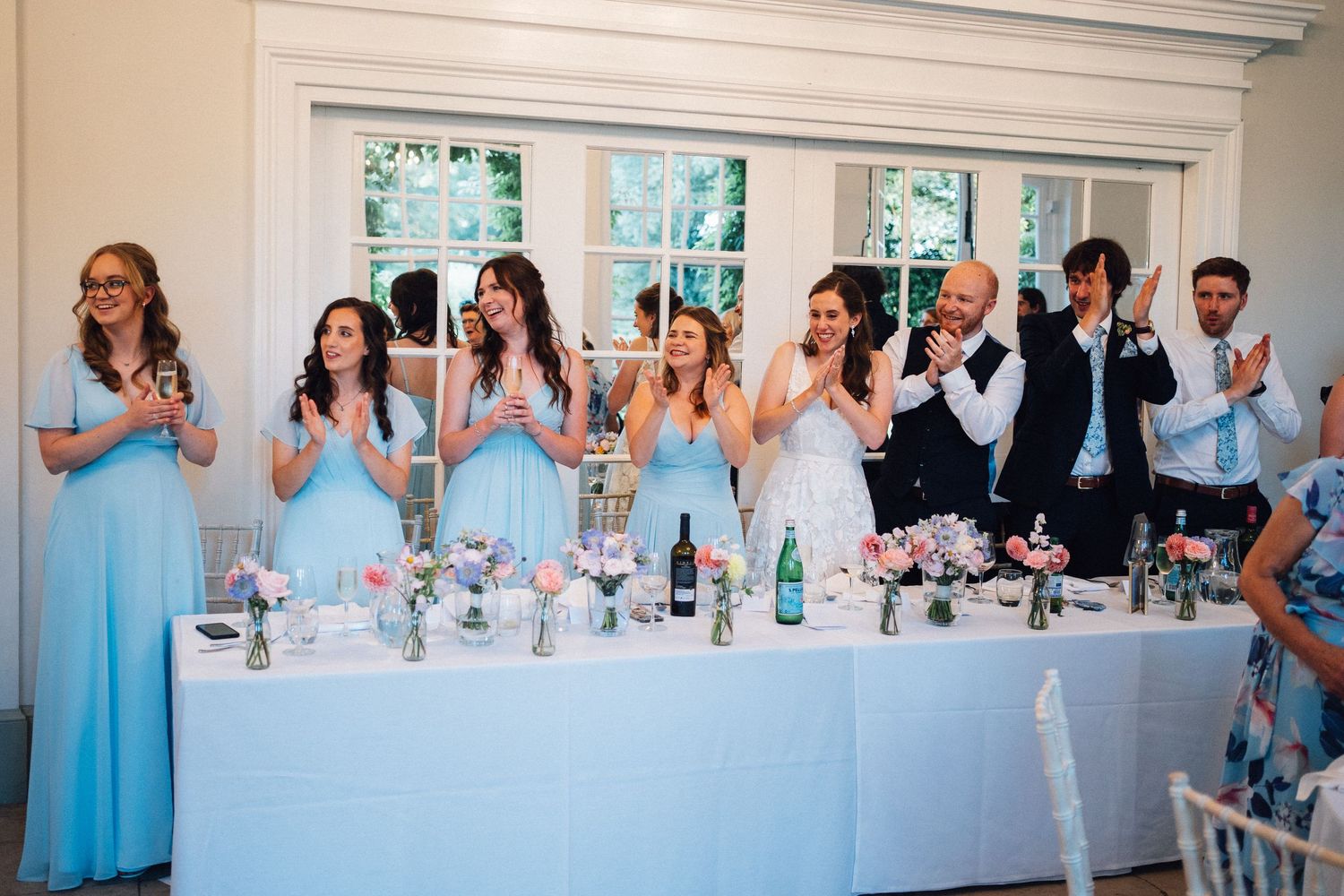 Wedding reception guests celebrating at long tables decorated in white linens.