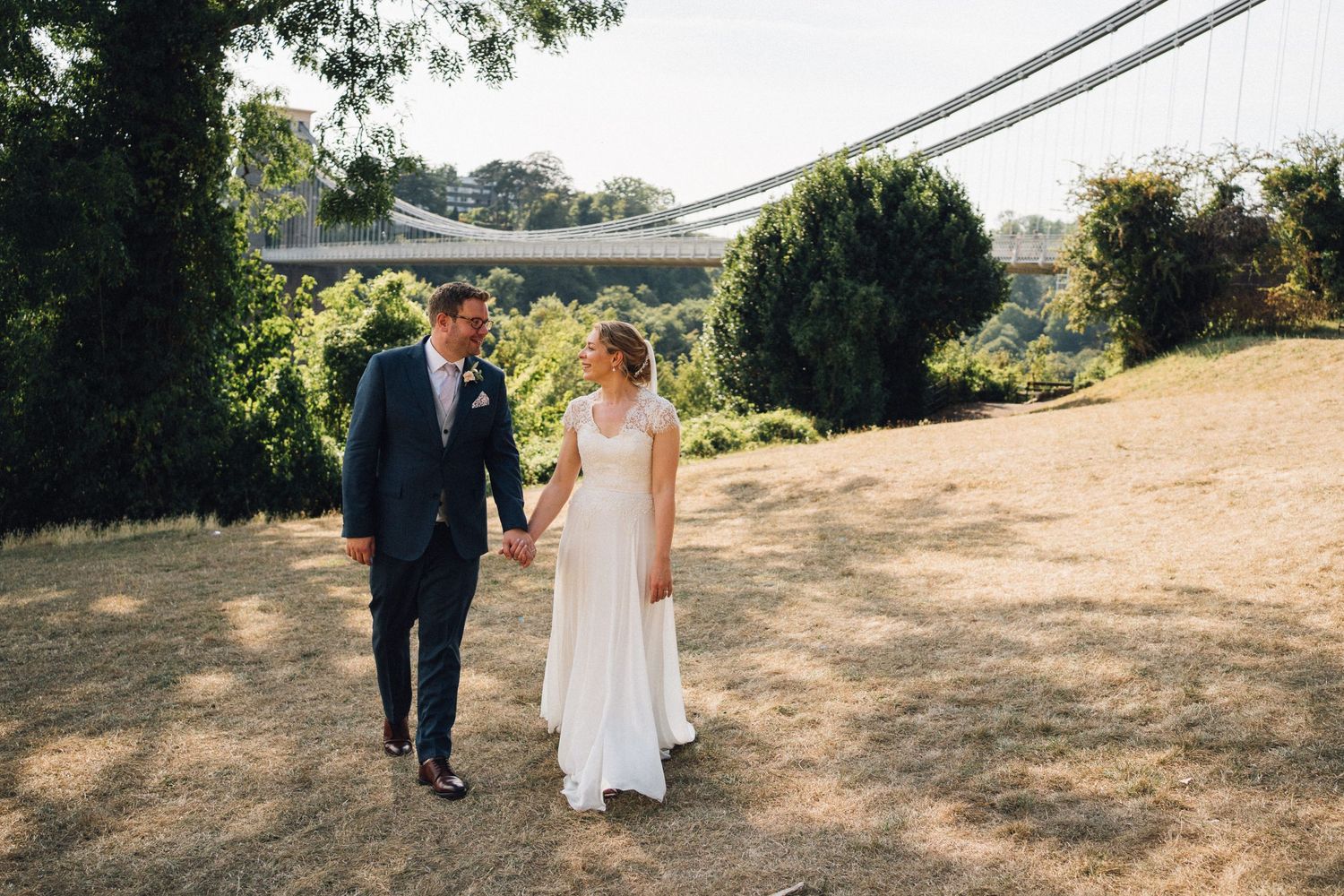 Wedding couple walks through a sunlit garden path on their special day.
