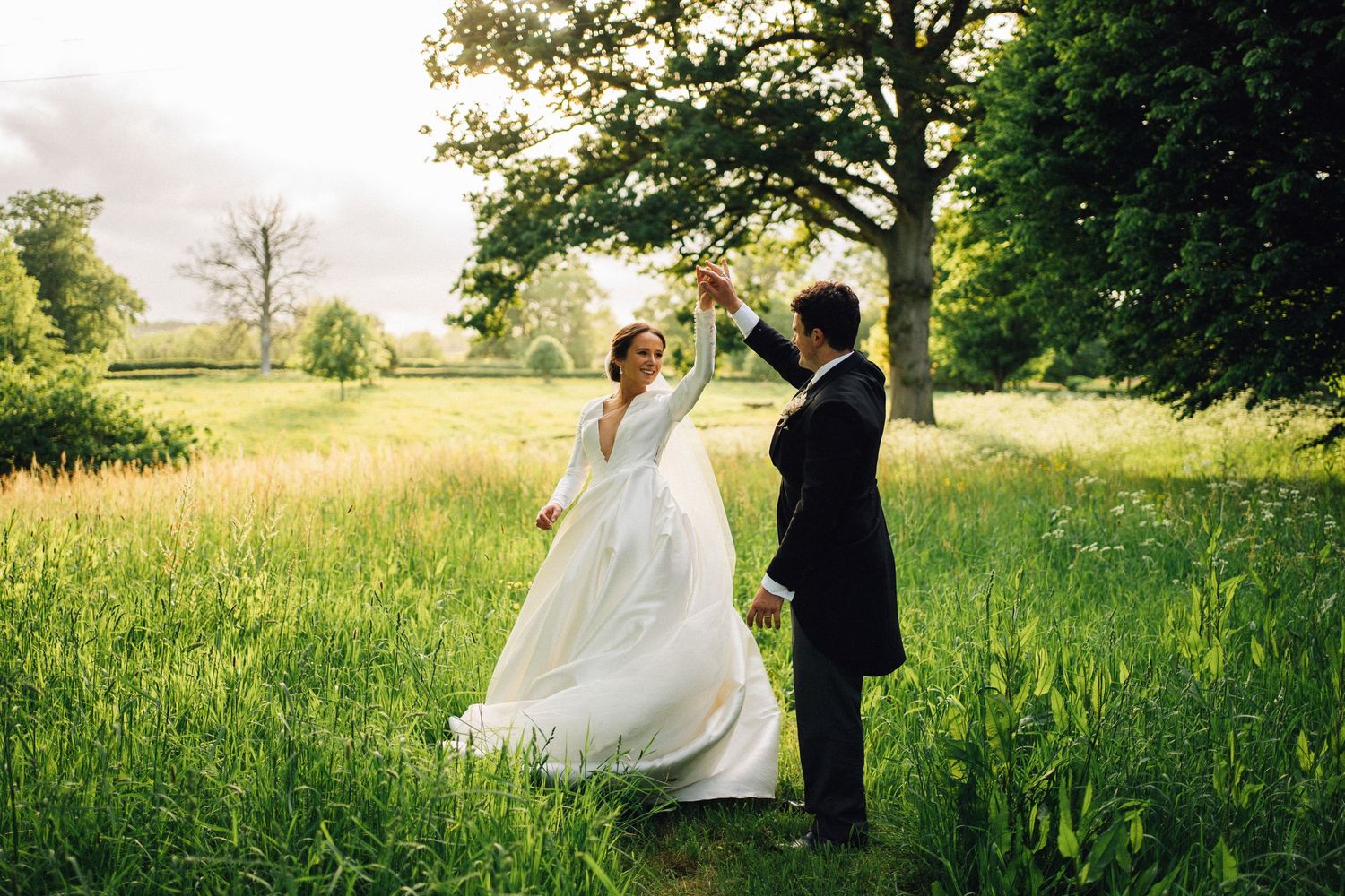 Wedding couple walking through a lush green meadow on a sunny summer day.