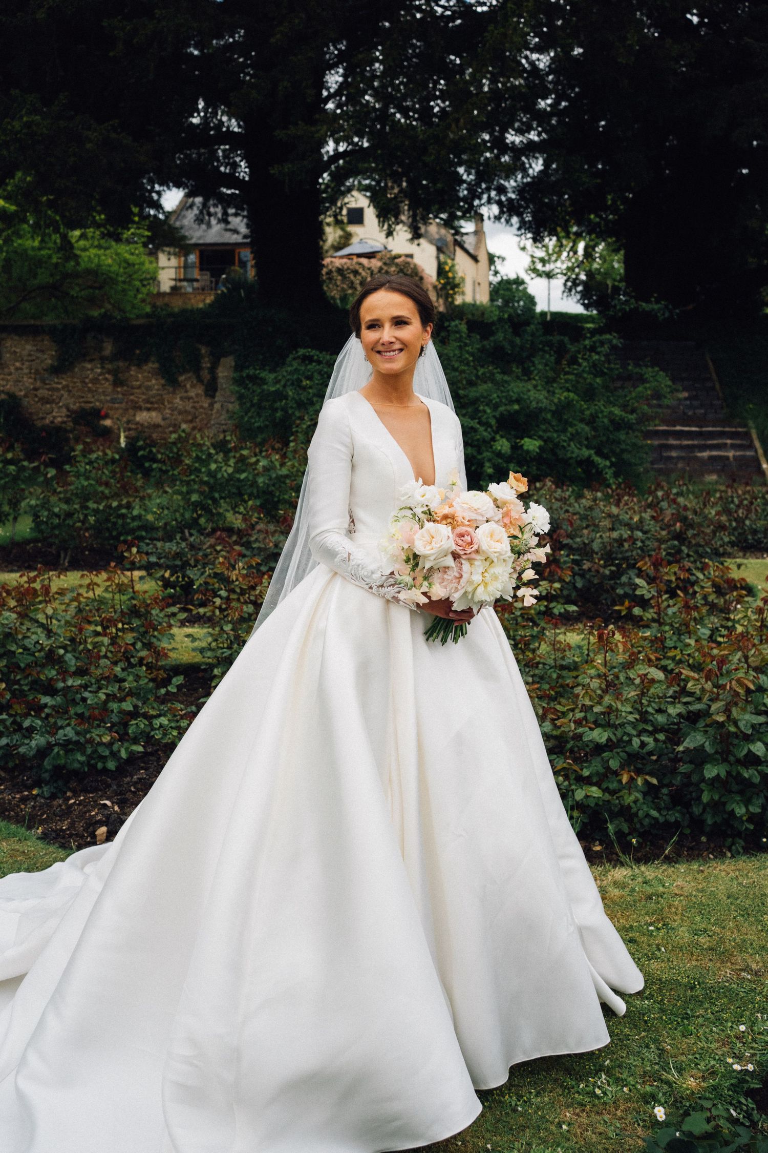 Elegant white wedding gown with full skirt photographed in garden setting.