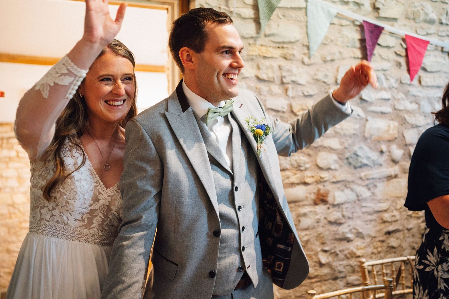 Wedding guests seated at rustic stone wall venue decorated with colorful bunting and sunflowers.