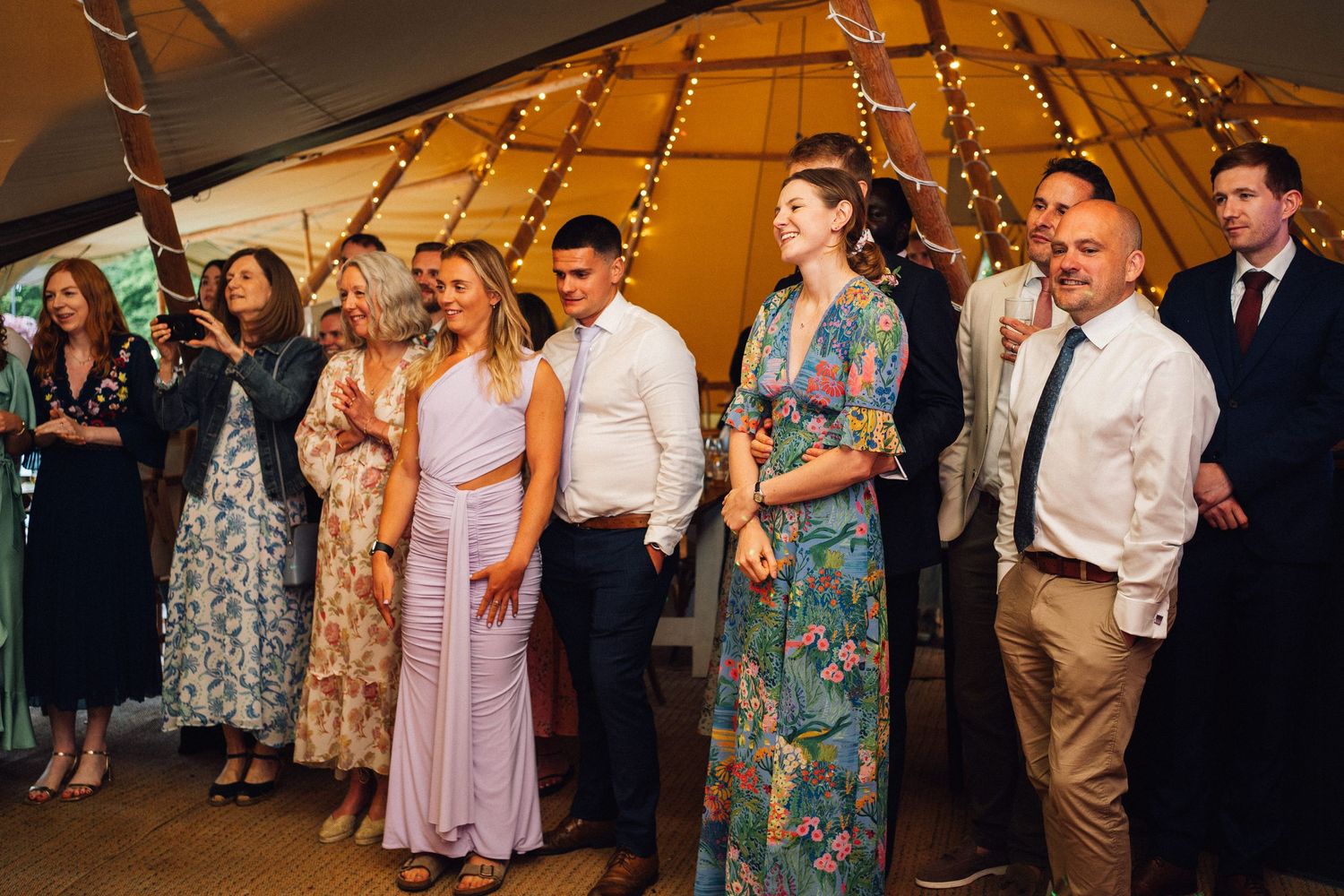 Wedding guests dancing and celebrating at reception under yellow tent lighting.