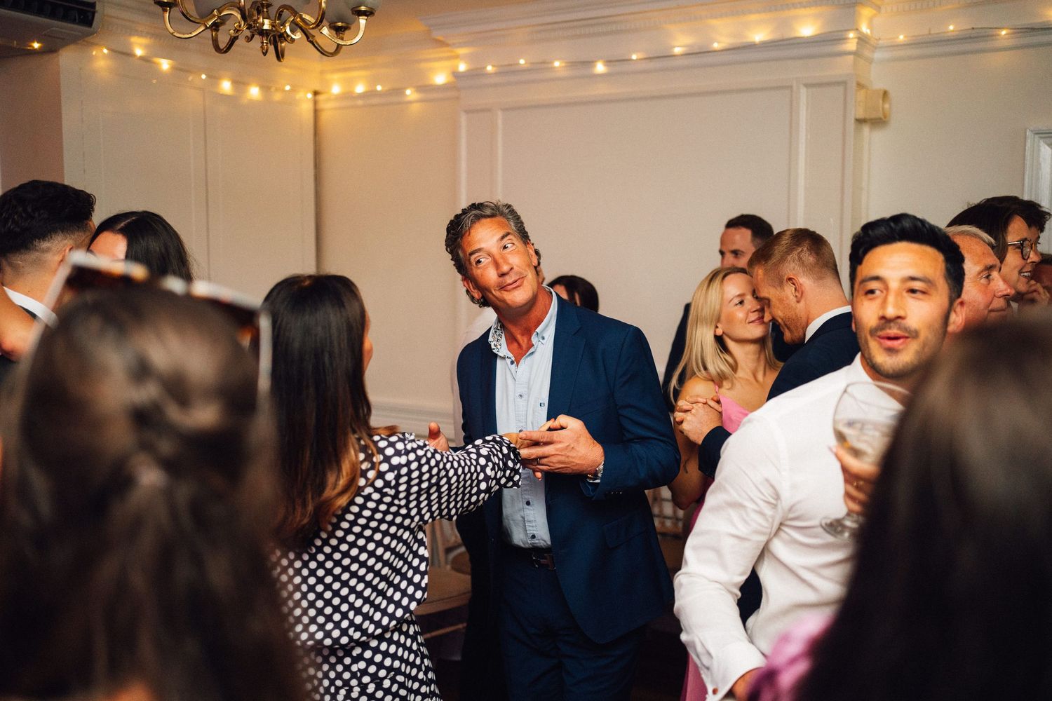 Wedding reception dance party with string lights and chandelier creating festive atmosphere.
