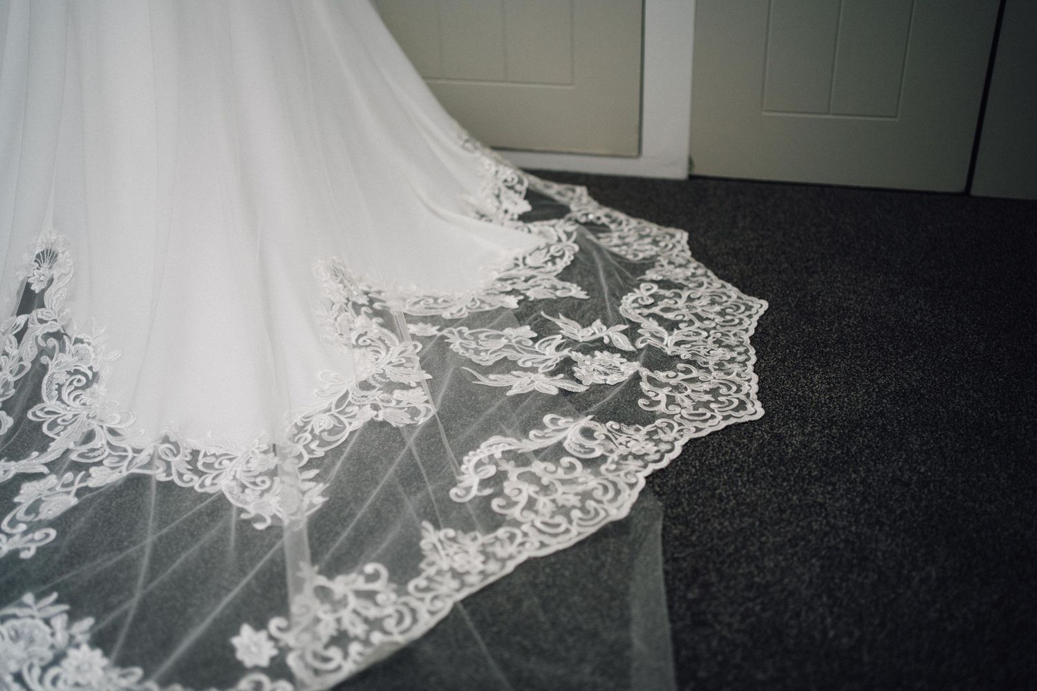 Delicate lace detail of wedding dress veil against dark background.