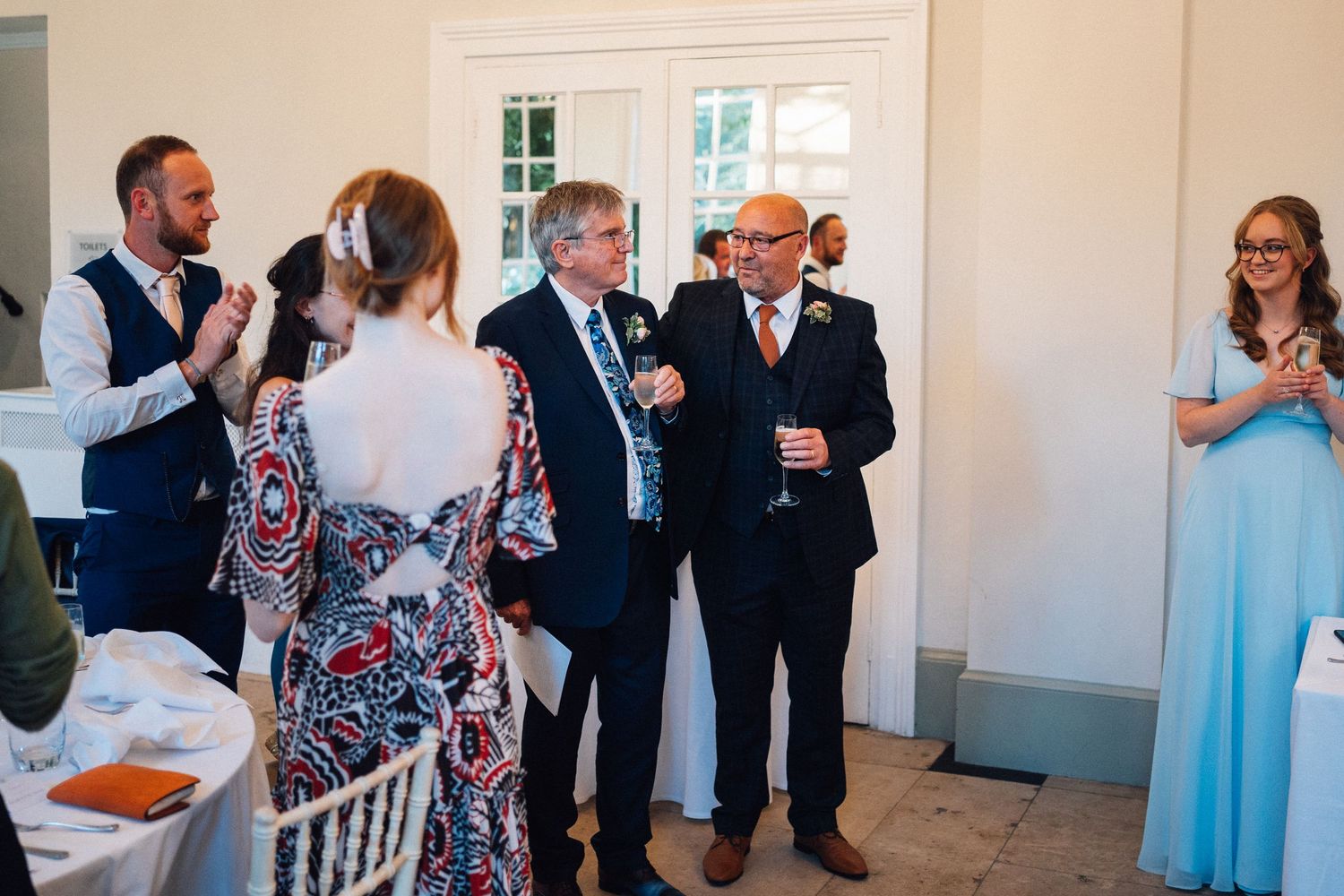 Indoor wedding reception with guests mingling and celebrating in an elegant white room.