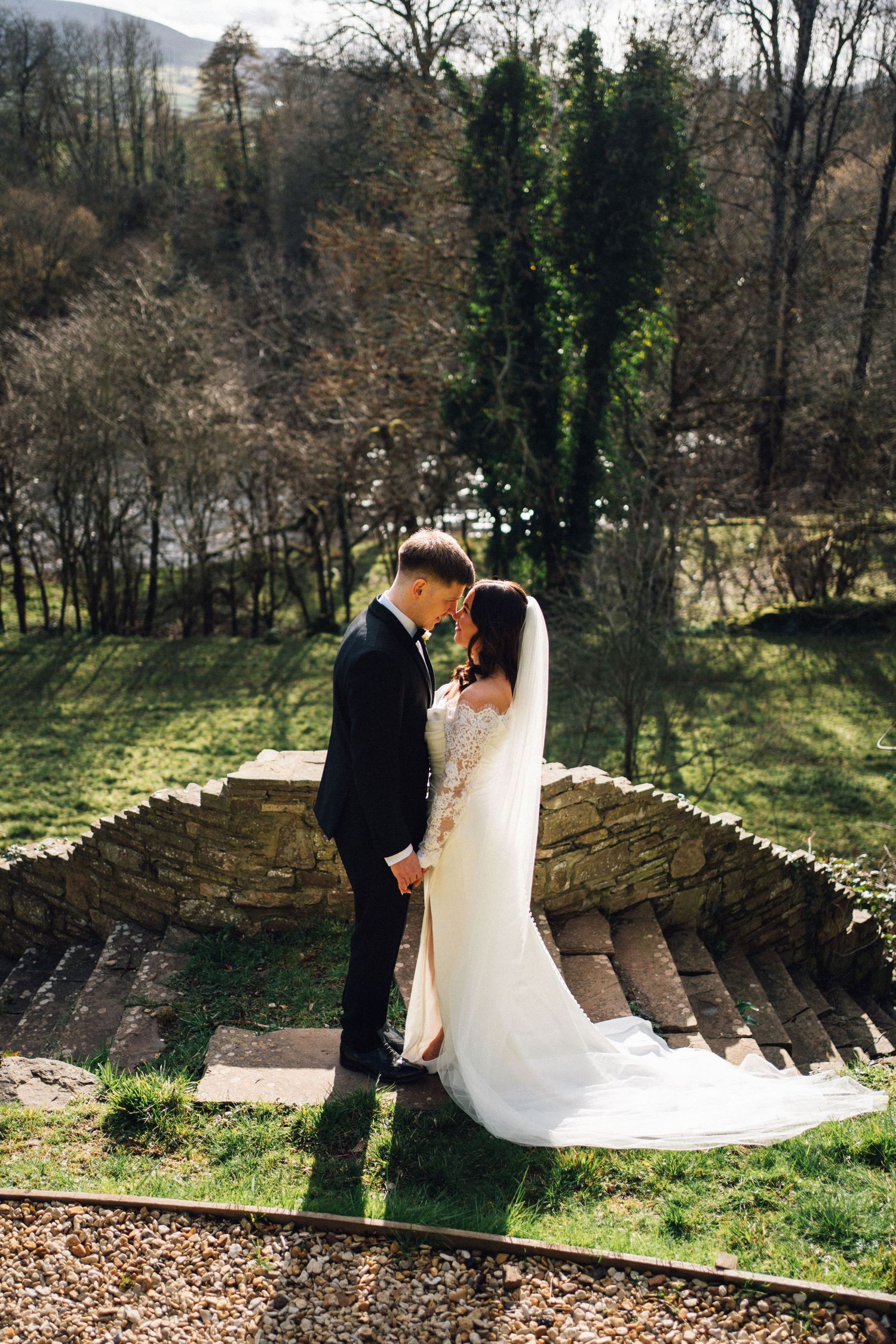 Bride and groom share romantic moment on stone steps surrounded by lush greenery on their wedding day.