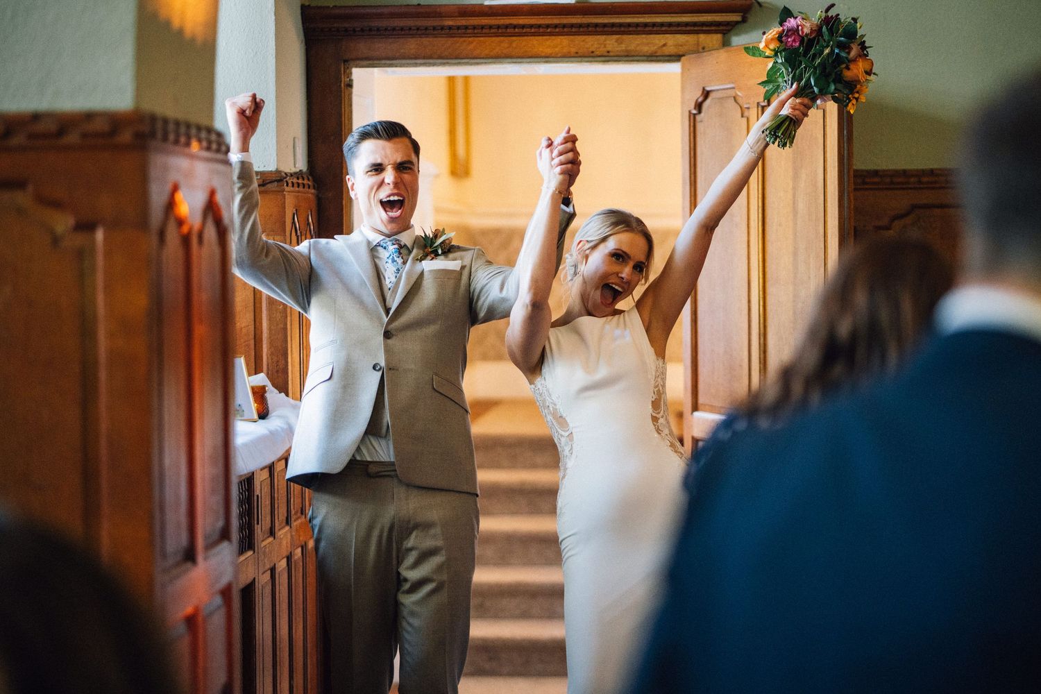 Wedding celebration in a wood-paneled room with guests raising their arms in celebration.