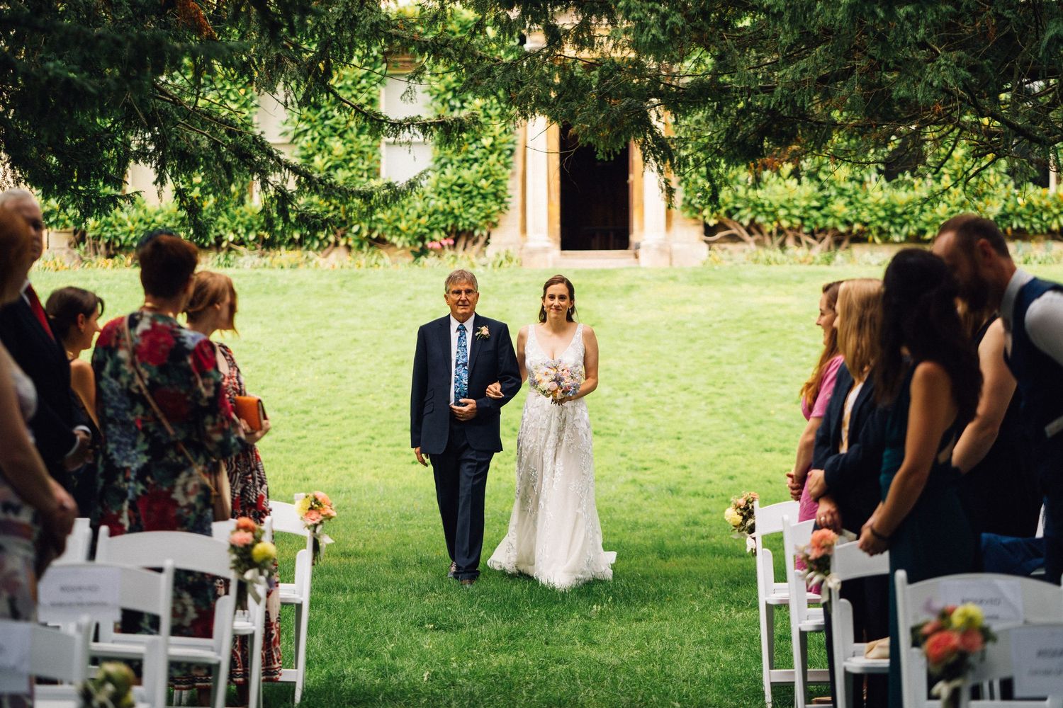 Garden wedding ceremony setup with white chairs and lanterns along a grassy aisle.