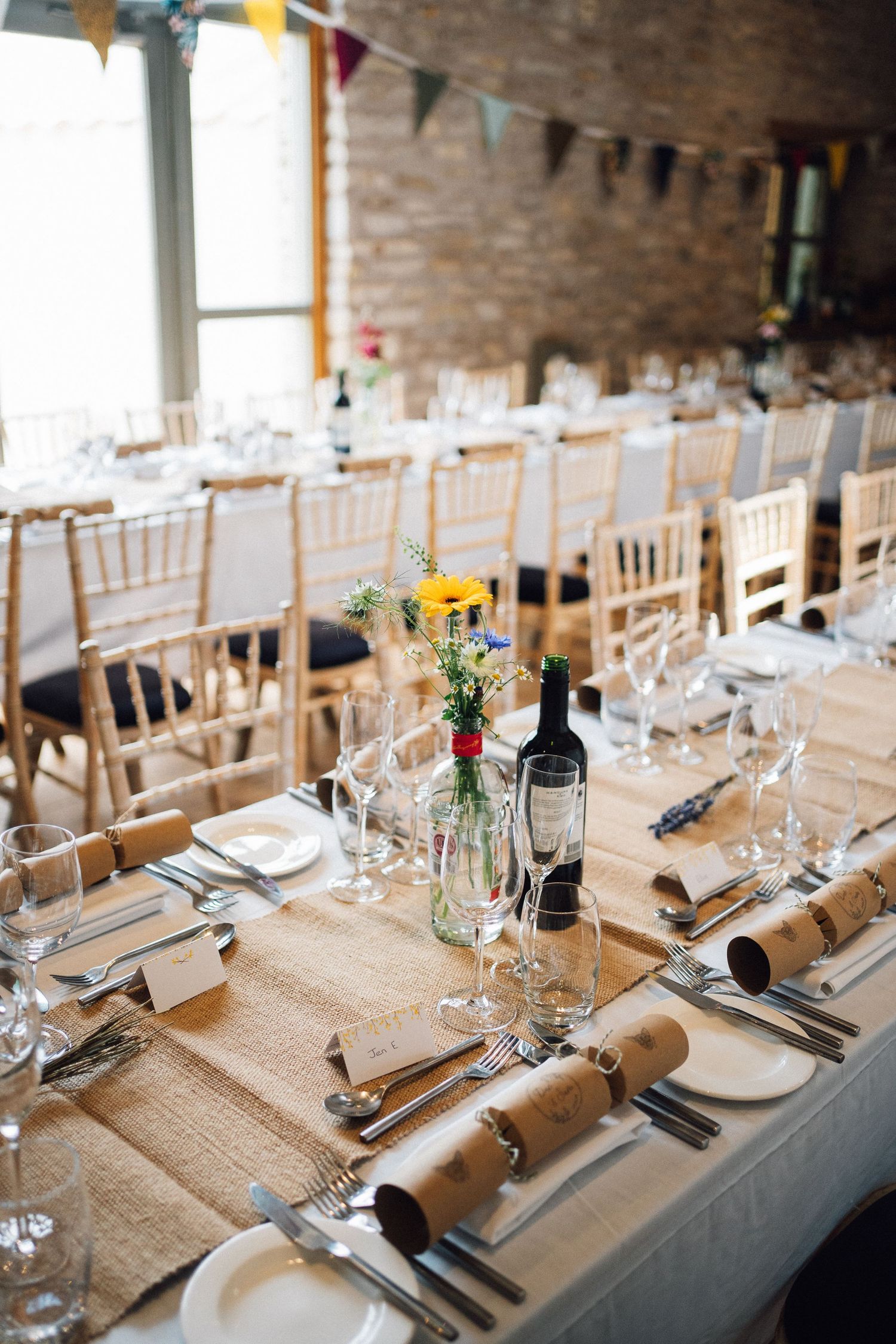 Rustic wedding reception tables with burlap runners and colorful bunting decorations.
