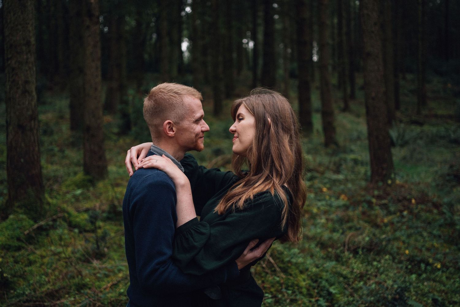 Romantic forest photoshoot with couple embracing among evergreen trees.