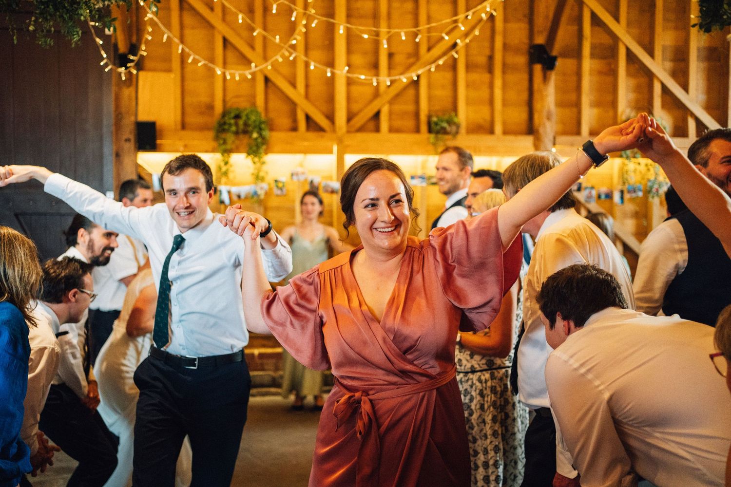 Wedding guests dancing and celebrating in rustic barn venue illuminated by string lights.