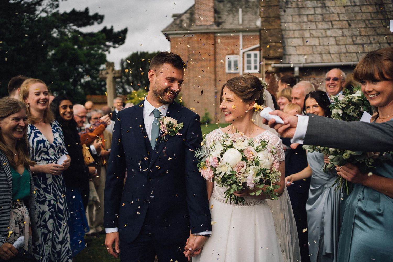 Wedding celebration outside with guests throwing confetti in joyful celebration.