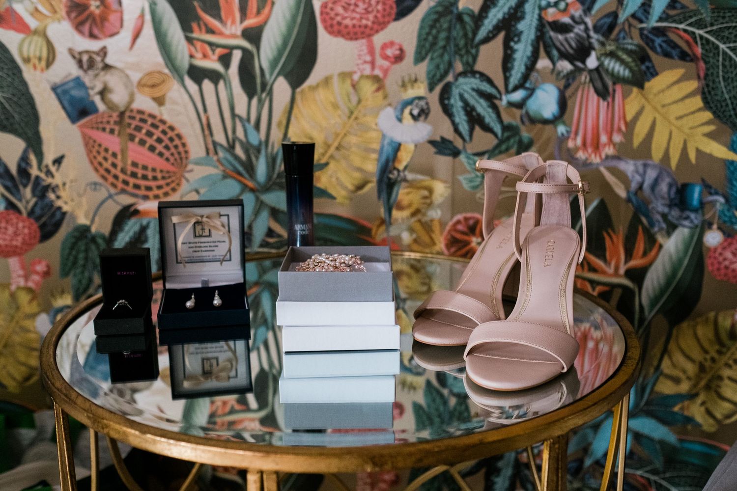 Wedding accessories displayed on a gold mirrored table with floral wallpaper background.