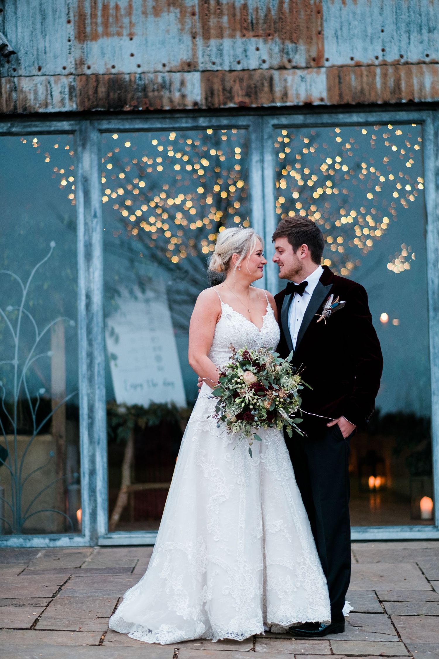 Wedding portraits featuring elegant white dress against weathered blue wall with string lights.
