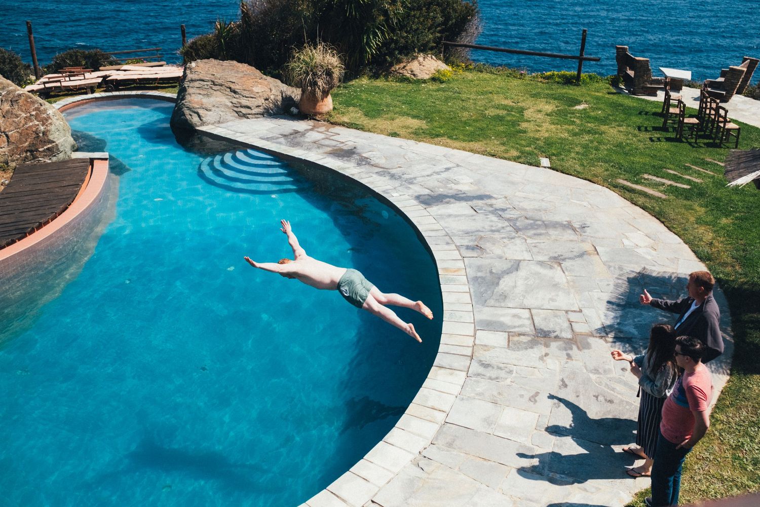 Swimming pool with curved edges overlooking ocean views and stone patio.