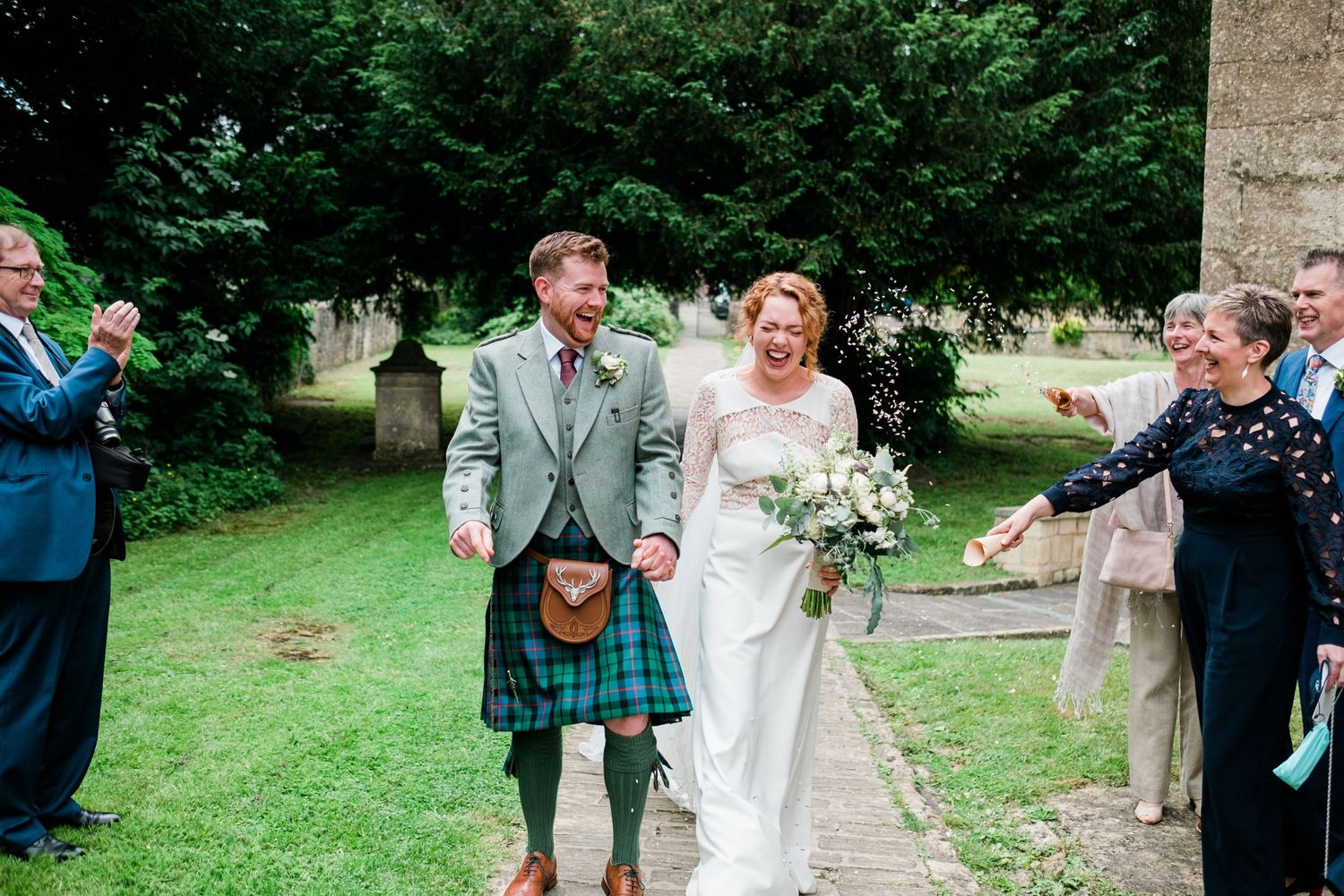 Wedding couple walking on garden path while guests celebrate with confetti.