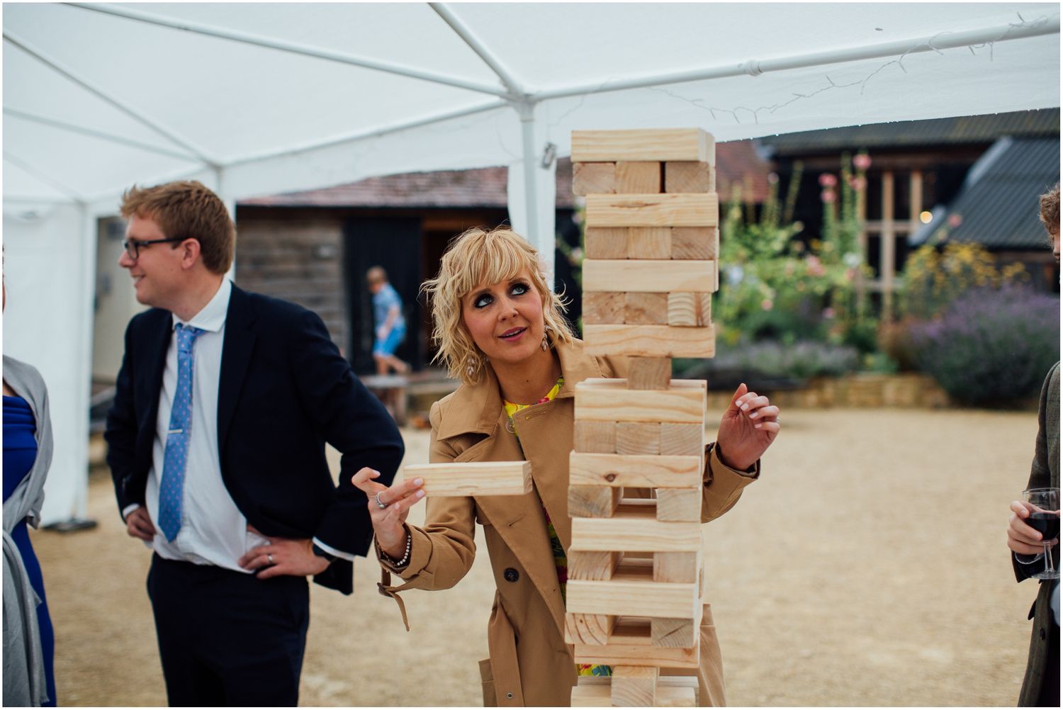 Wedding guests gathered around large wooden Jenga tower during outdoor reception.