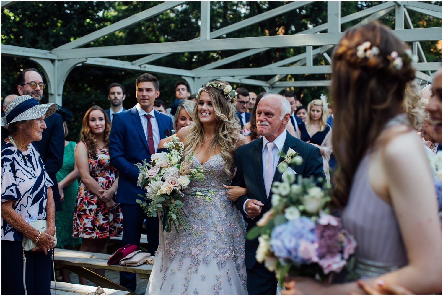 Wedding ceremony taking place under white pergola with guests watching.