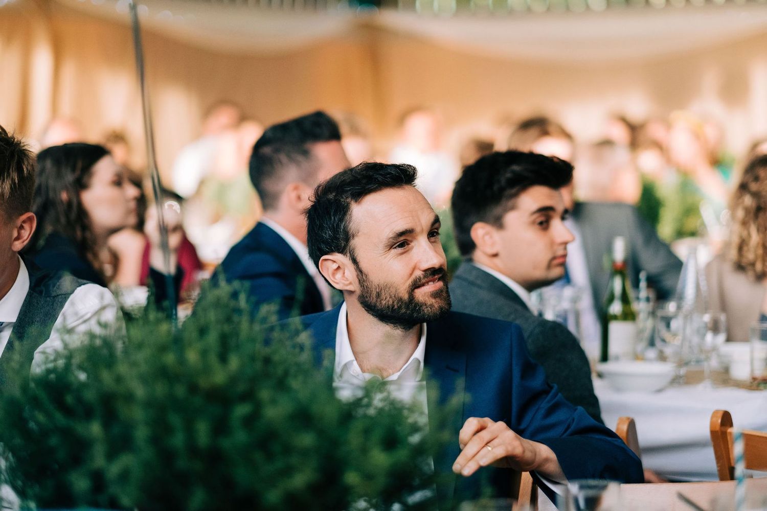 Guests seated at elegant tables decorated with greenery at a wedding reception.