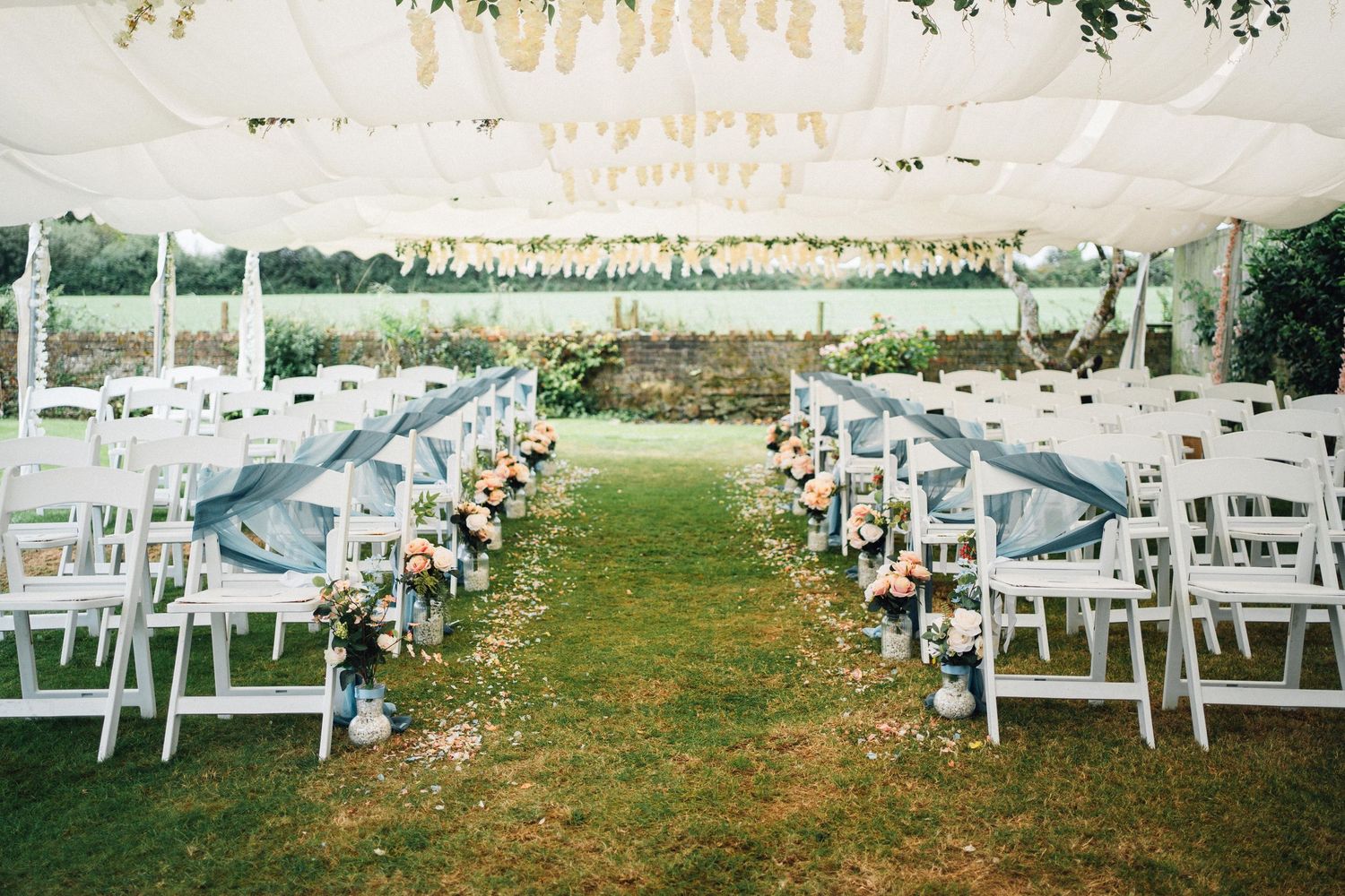 White wooden chairs arranged in rows on a grassy lawn for an outdoor wedding ceremony.