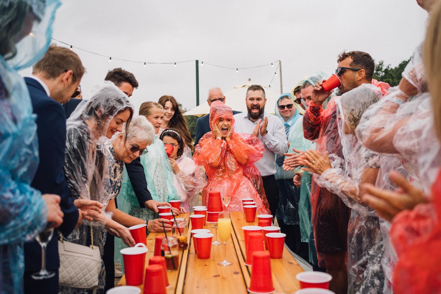 People playing flip cup at a party with red plastic cups lined up on a long table.