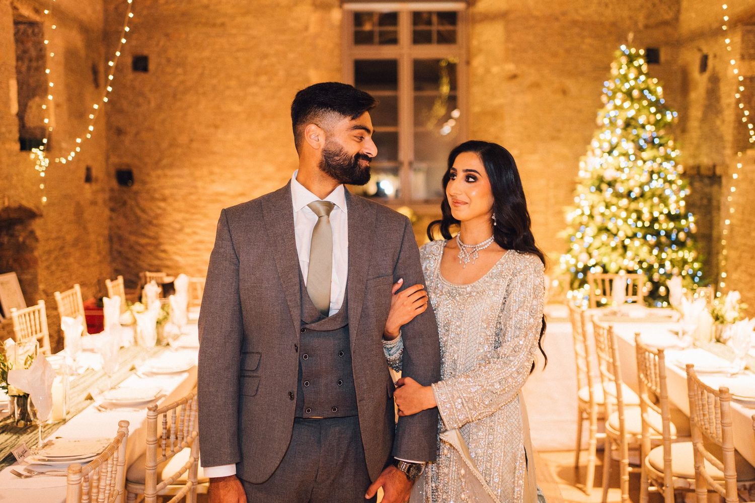 A romantic winter wedding reception with twinkling lights and Christmas trees in a rustic brick venue.