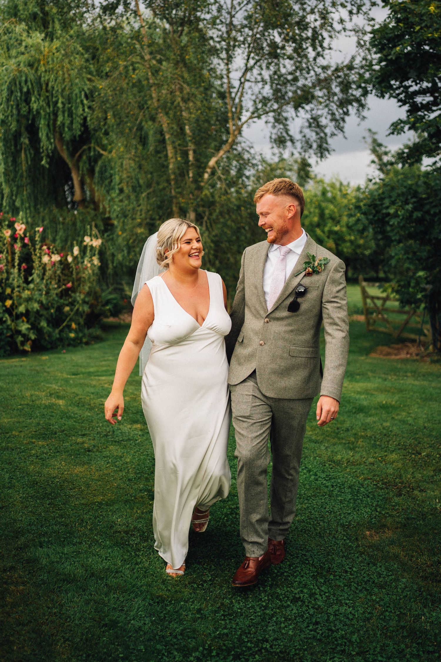 A couple walks together on a lush green lawn during what appears to be a wedding celebration.