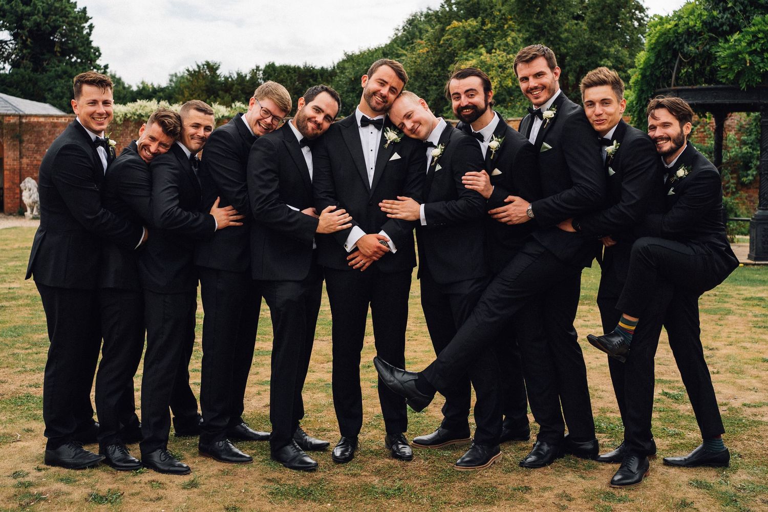 A group wearing black suits poses together outdoors in a series of candid photos showing playful interactions.