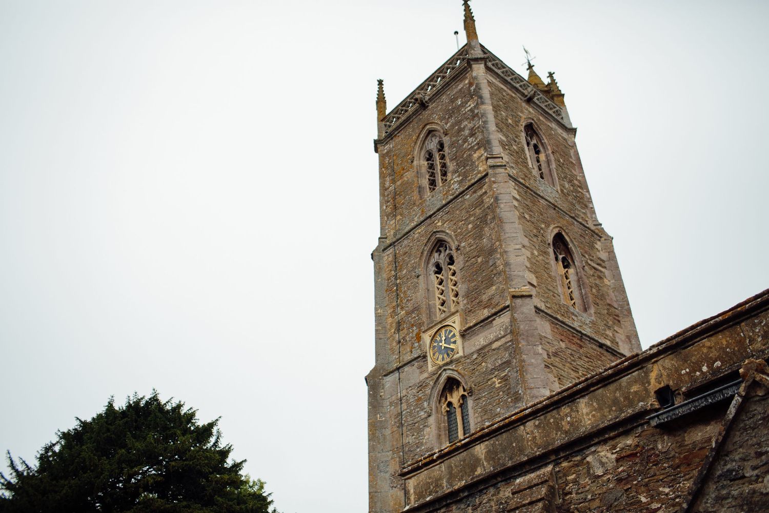 Historic stone church tower with gothic architectural details rises against cloudy sky in English countryside.
