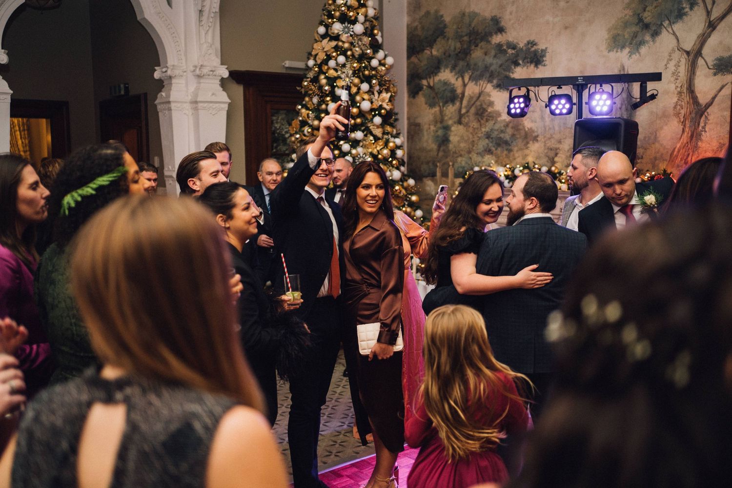 Wedding reception dance floor filled with guests celebrating under ornate chandeliers and Christmas lights.