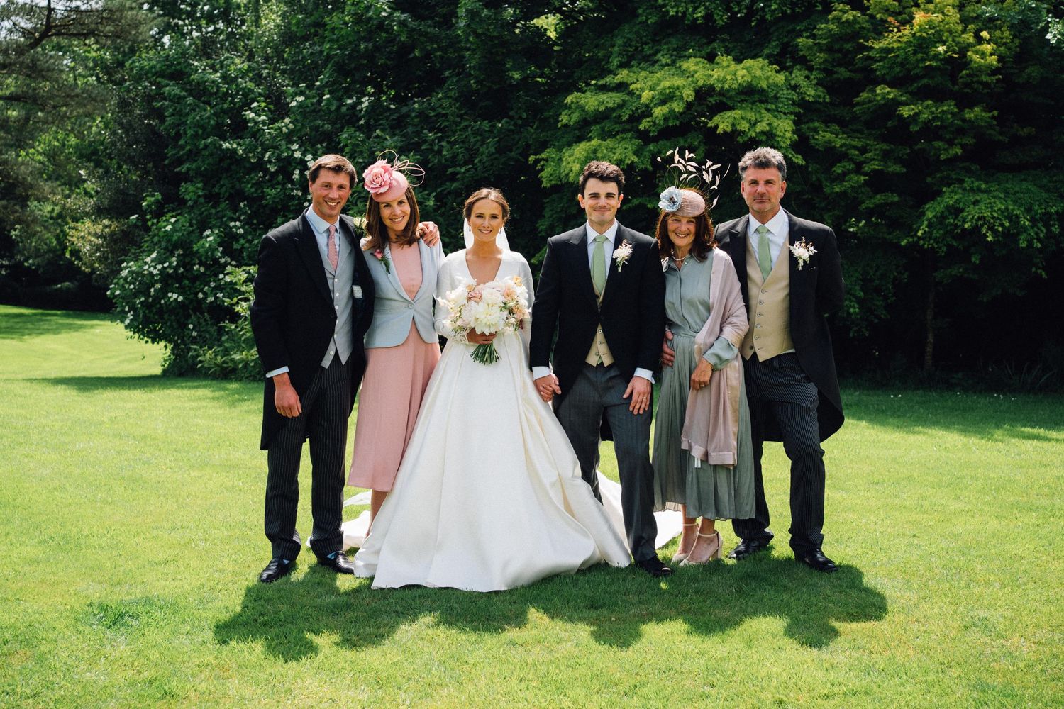 Wedding party members pose together on a lush green lawn during an outdoor celebration.