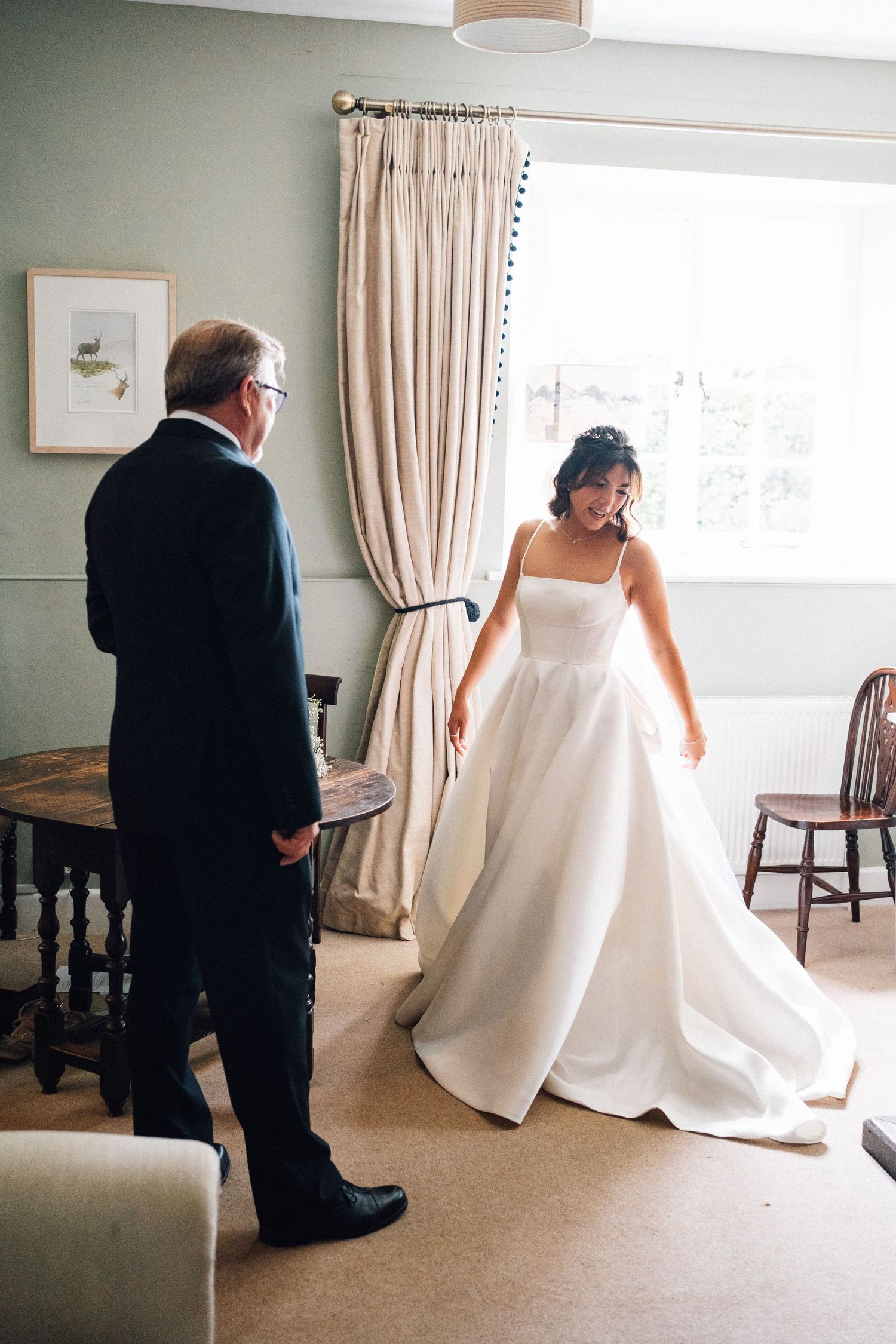 A person in a suit watches as someone in a wedding dress twirls in an elegant room.