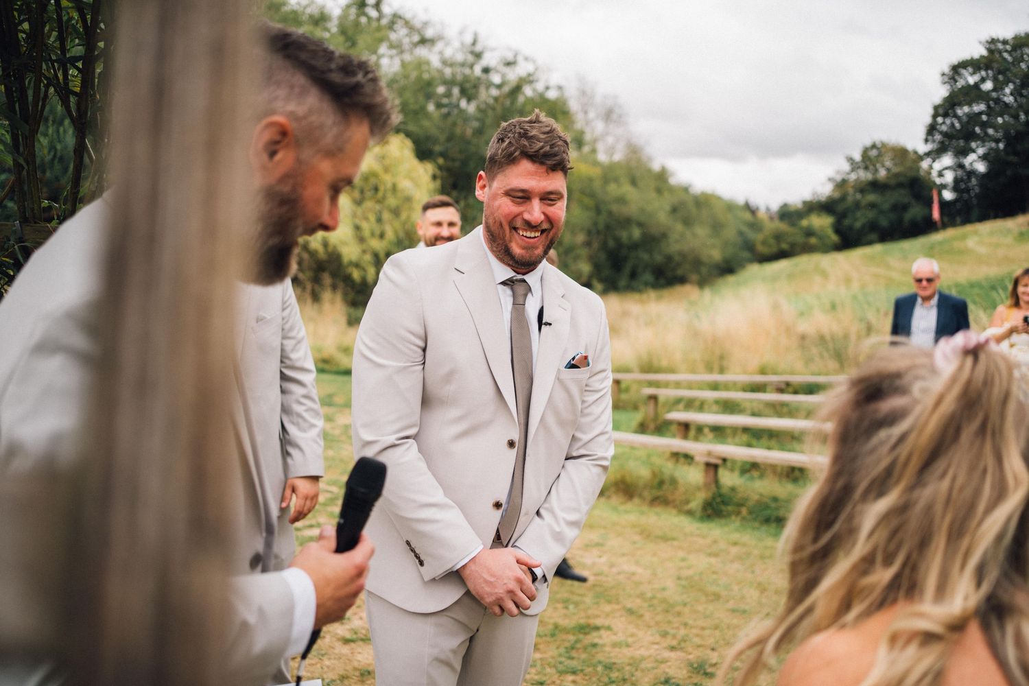 Wedding party members in light colored suits gather during an outdoor ceremony.