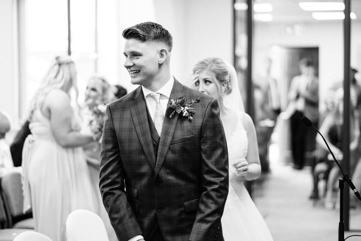 Black and white photo capturing a joyful moment during an indoor wedding ceremony.