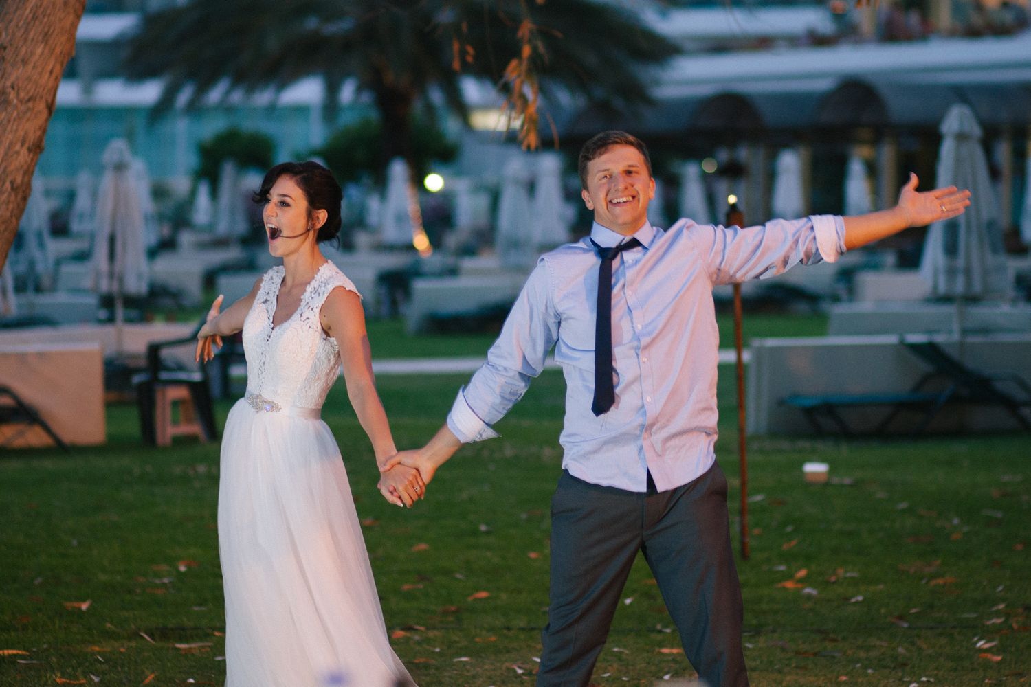 A couple dances playfully on grass during their wedding celebration.
