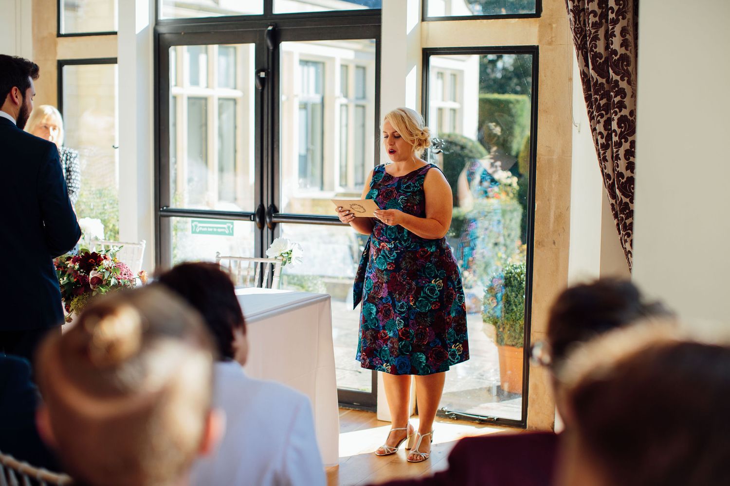 Guests watch attentively during an indoor wedding ceremony with sunlight streaming through windows.