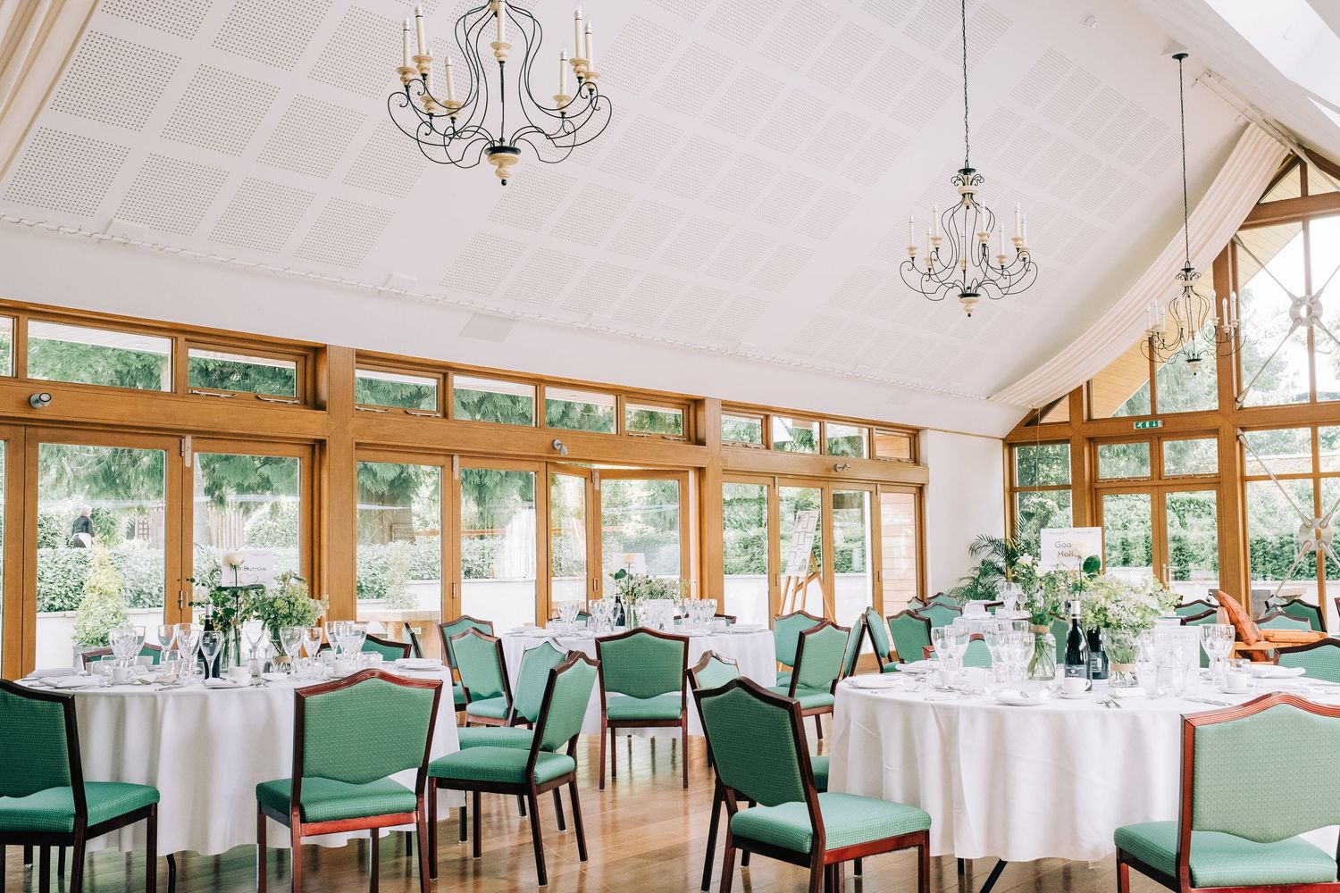 An elegant reception room with white tables, green chairs, and crystal chandeliers.