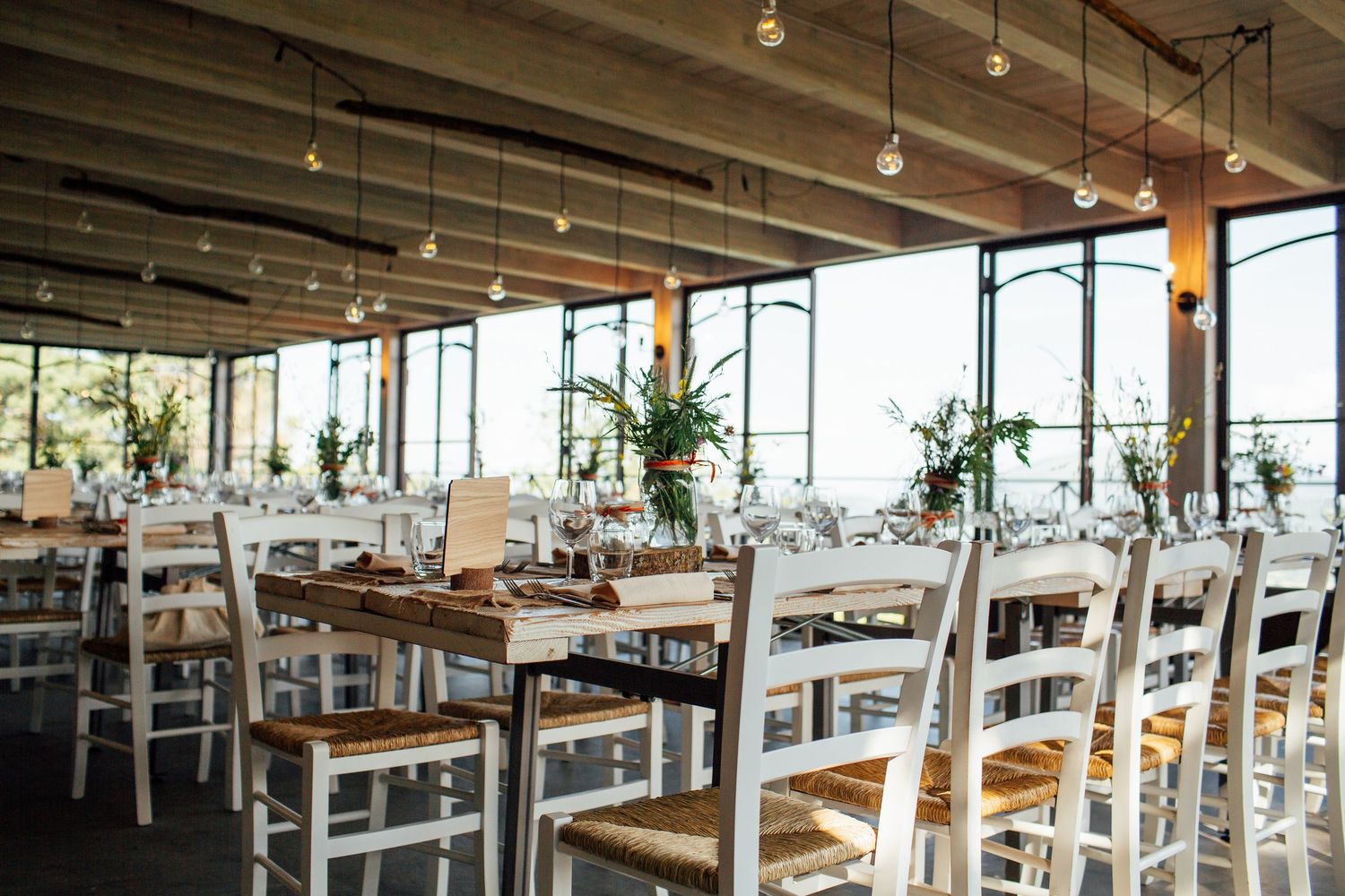 Modern rustic wedding reception venue with industrial ceiling and large windows letting in natural light.