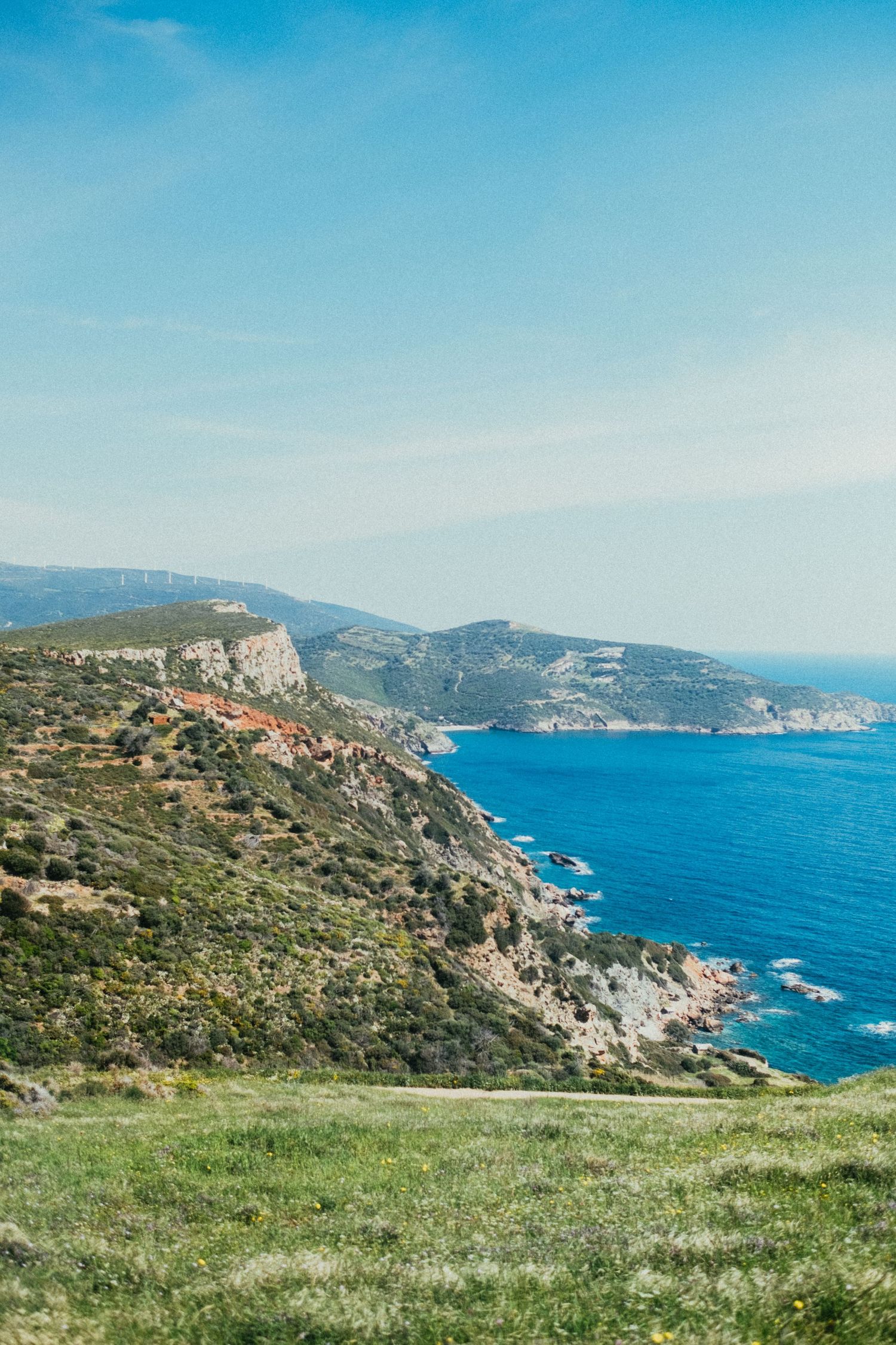 Panoramic coastal landscape with green hills and cliffs overlooking deep blue Mediterranean waters.
