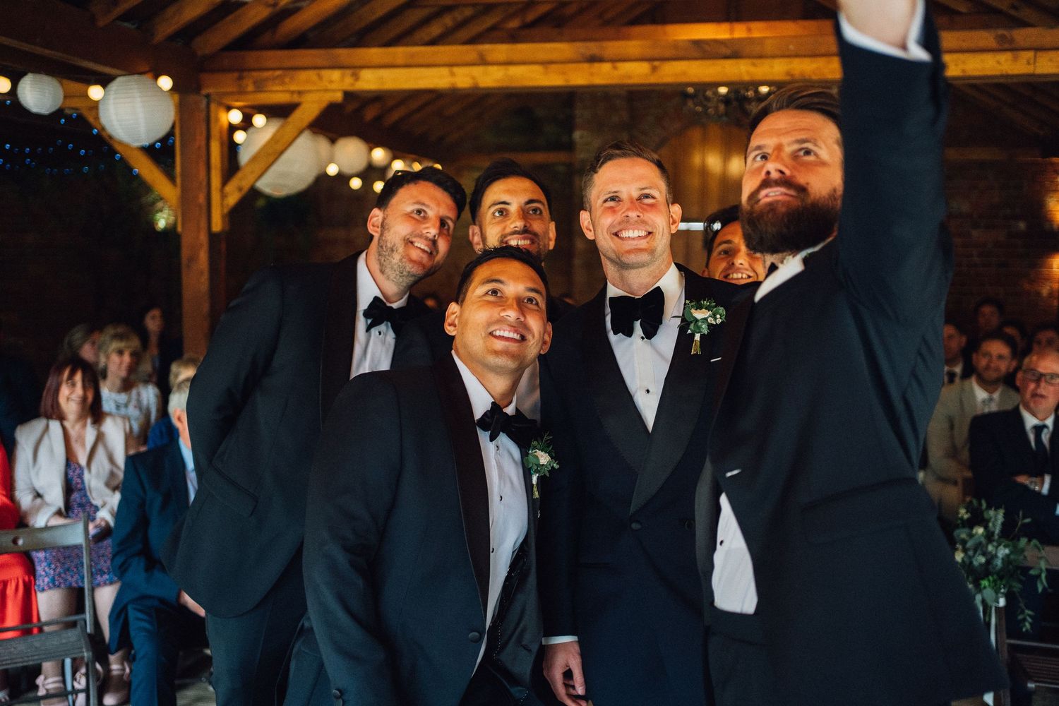 Wedding guests in formal attire laugh and celebrate during a joyous reception in a rustic wooden venue.