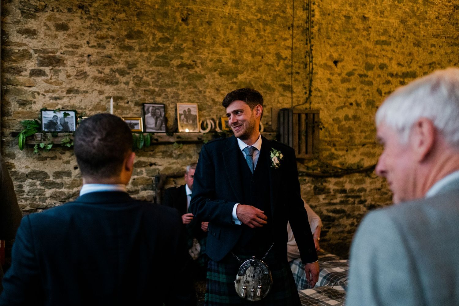 Wedding guests mingling in front of rustic stone wall during evening reception.