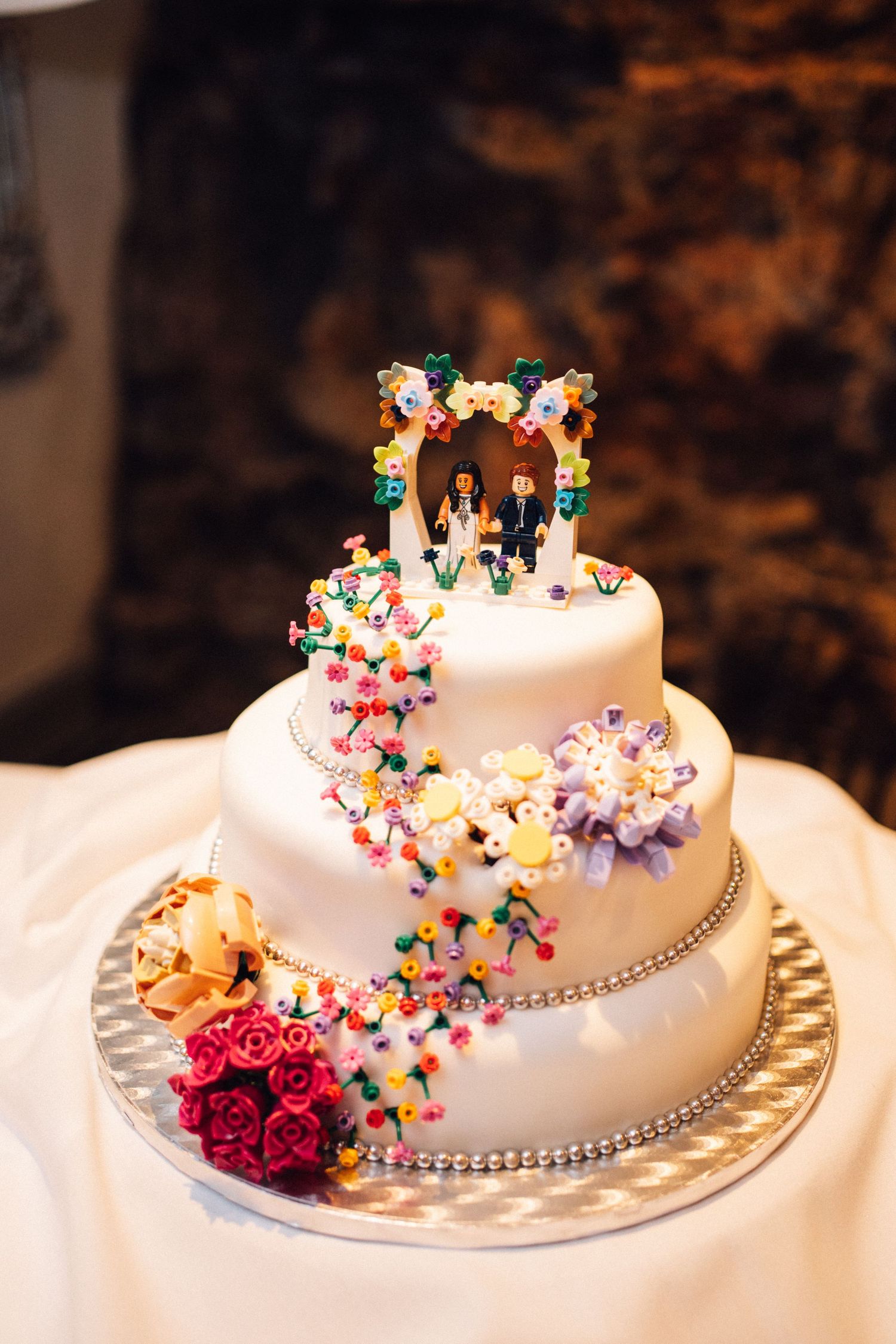 White wedding cake decorated with cascading colorful butterflies and red roses on a gold plate.